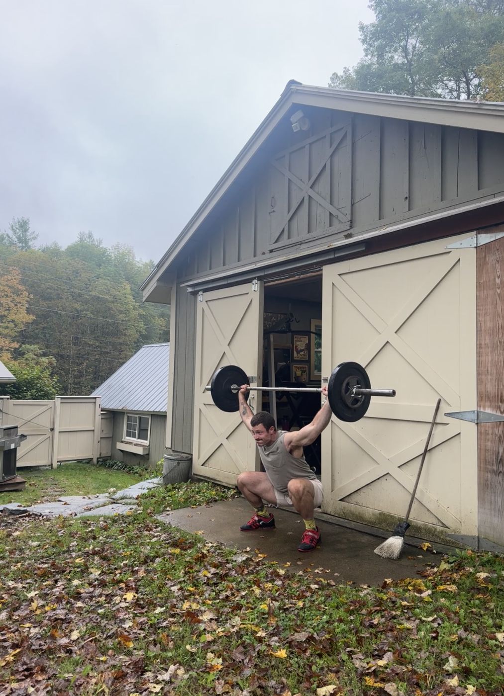 Tanner Wright holding a barbell in an overhead squat outside his barn gym in Vermont